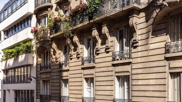 A multi-story building with ornate balconies, large windows, and a ground-level entrance.