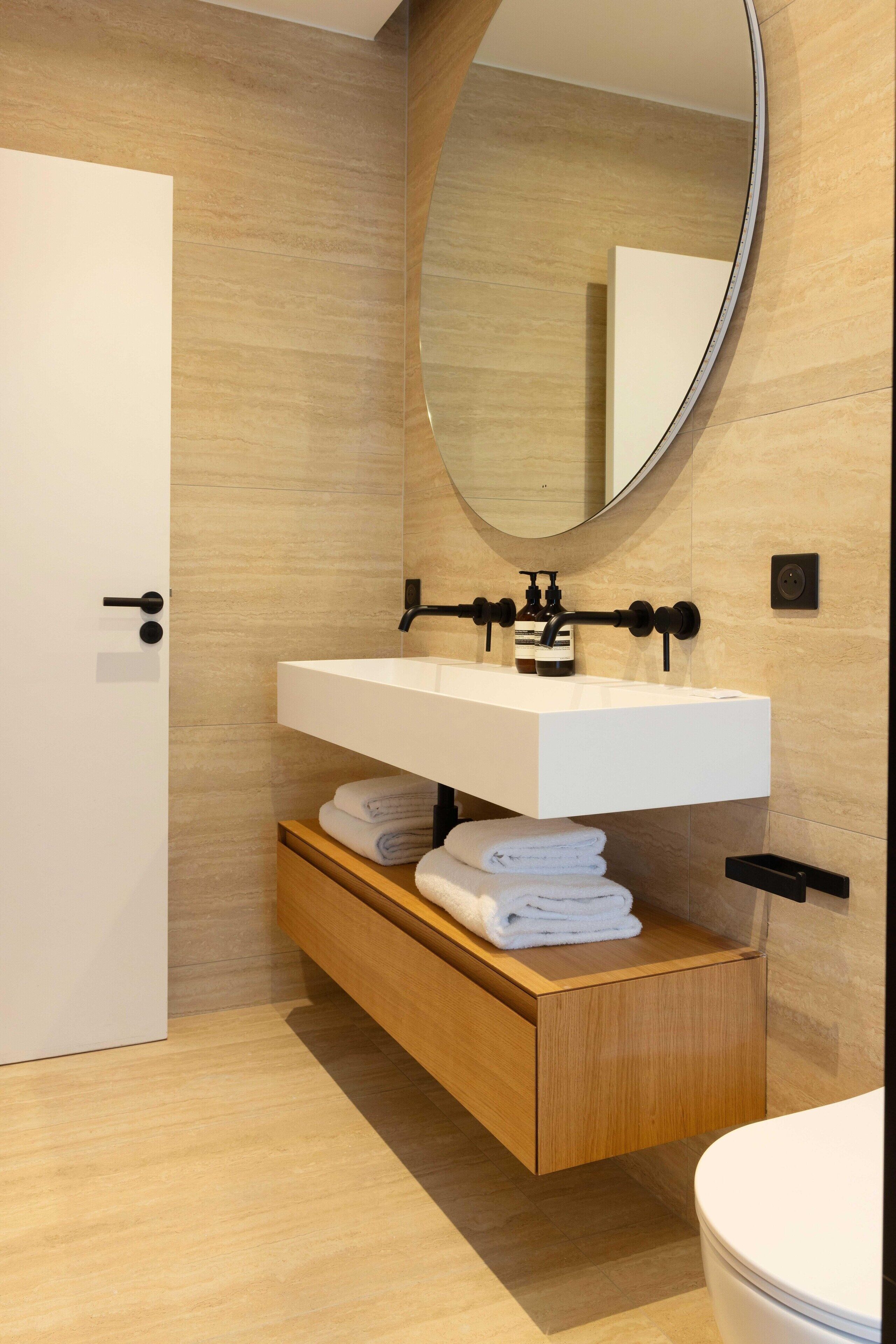 Een moderne badkamer met een wit wastafel, houten opbergmeubel en een grote spiegel.