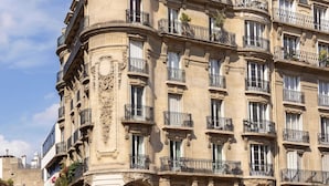 A historic building with multiple balconies, a corner turret, and storefronts including a junior center and a photography service.