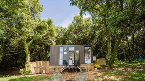 Una cabaña moderna y compacta con terraza, asientos exteriores y una pequeña mesa.