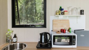 Una cocina con un lavamanos, una tetera, un microondas y una ventana con vistas a árboles.