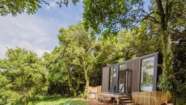 Una cabaña moderna con terraza, rodeada de un bosque frondoso.