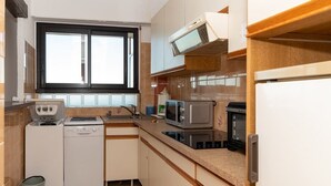 A compact kitchen with a dishwasher, microwave, and stove. - Location d'un studio cabine pour 4 personnes face mer, centre ville. (LE LAVANDOU)