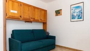 A teal sofa in a room with wooden cabinets and a small framed picture on the wall. - Location d'un studio cabine pour 4 personnes face mer, centre ville. (LE LAVANDOU)