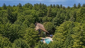 Una casa circondata da un fitto bosco, con vista libera su un ampio specchio d'acqua e montagne lontane.