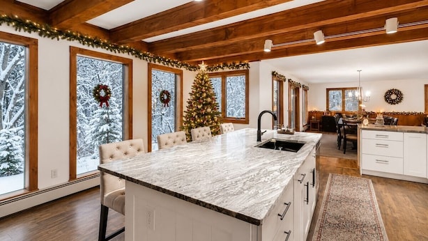 Una cucina moderna con isola in marmo, travi in legno, ampie finestre e un albero di Natale.