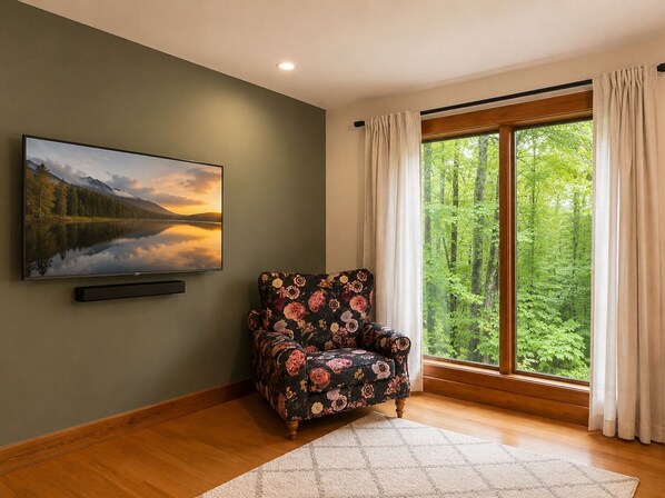 A room with a large window, a chair, a flat-screen TV, and a painting. - Private Pool & Hot tub! Minutes to Sebago Lake! Nature! Perfect all year-round. (Windham)