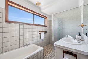 Bathroom features a large bathtub, vanity with mirror, and window above the sink.