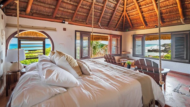 Een slaapkamer met een bed, een stoel, een tafel en uitzicht op zee.
