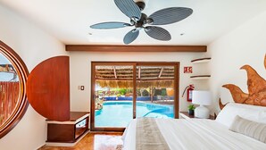 A hotel room with a bed, a ceiling fan, a view of an outdoor swimming pool, and a fire extinguisher on the wall. - Bella Mar: Ocean Front w/ Pool Views (Isla Mujeres)