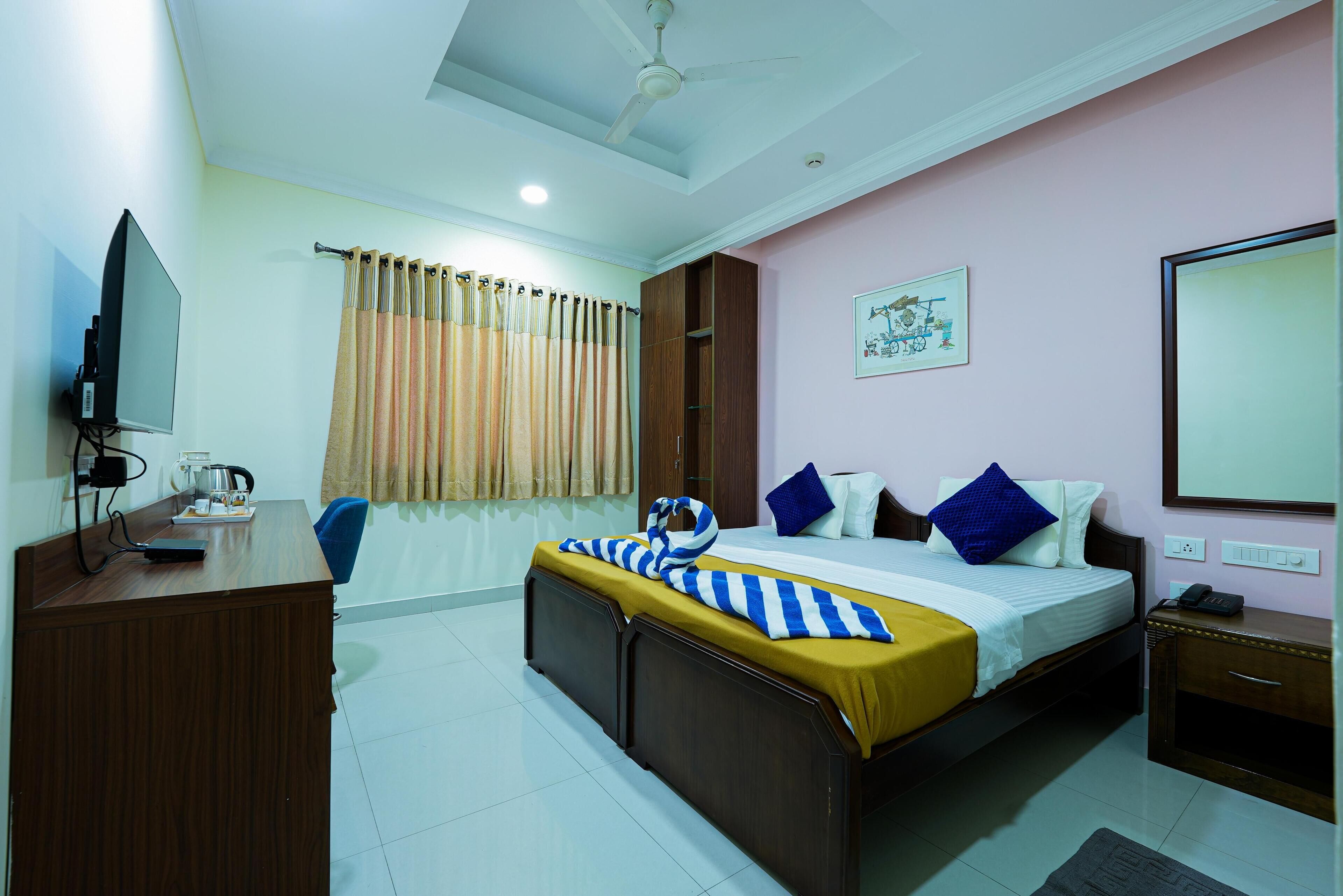 A hotel room with a bed, a desk, a TV, a window with curtains, and a ceiling fan.