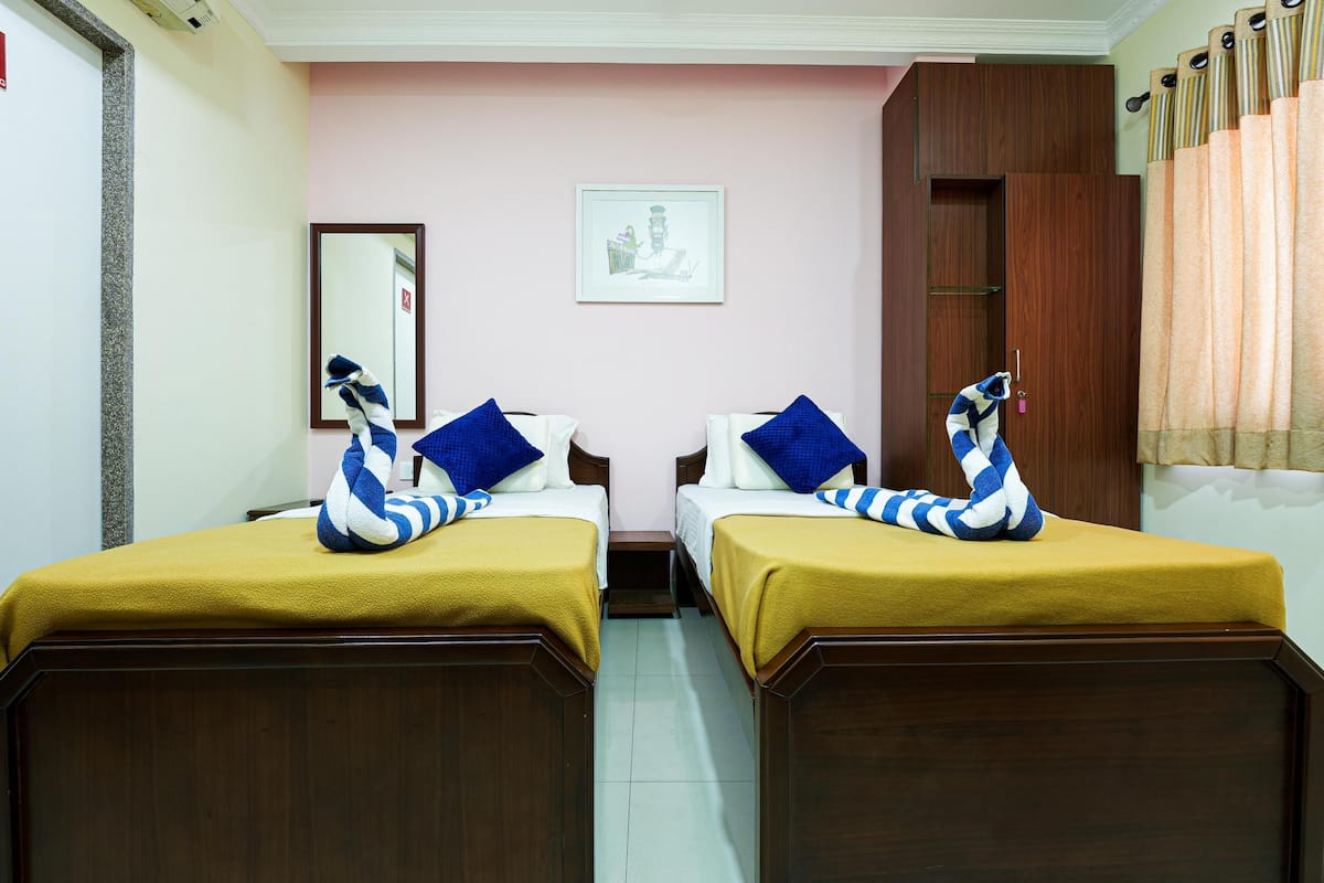 A hotel room with two beds, each with a blue and white striped pillow and a yellow bedspread. There is a wooden wardrobe and a framed picture on the wall.