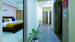 Une chambre d’hôtel avec un lit, une plante en pot et un couloir menant à un ascenseur.