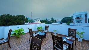 Une terrasse sur le toit, avec une table et des chaises, entourée de plantes en pot, et offrant une vue sur le paysage urbain.