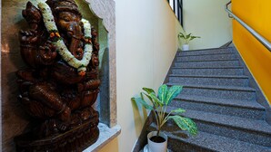 Un escalier orné d’une statue en bois sculpté représentant une divinité, un pot de fleurs et un mur jaune.
