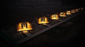 A row of small, uniformly designed cabins with individual lighting, arranged in a linear fashion on a flat landscape.