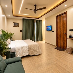 Una habitación de hotel con una cama, un televisor, un ventilador de techo, una puerta de madera y una cortina verde.