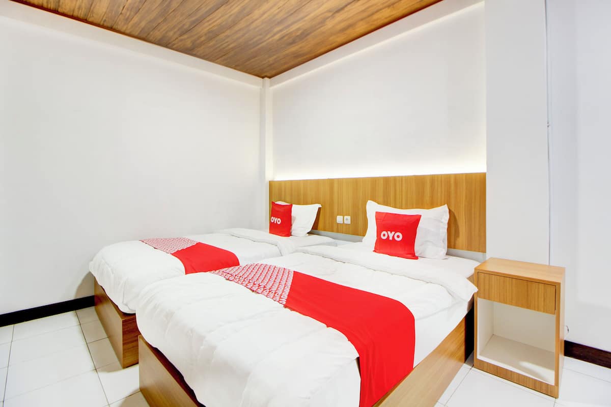 Une chambre d’hôtel moderne avec une tête de lit en bois, un grand lit avec une literie blanche et rouge, et une table de chevet.