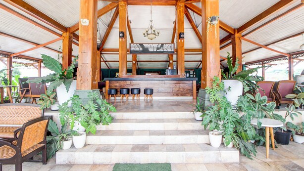 A covered outdoor seating area with wooden beams, a central counter, and potted plants.