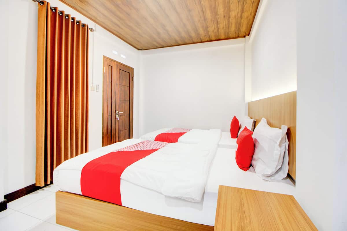 Une chambre d’hôtel moderne avec une tête de lit en bois, un grand lit avec une literie blanche et rouge, et une porte en bois.