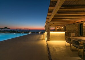 A poolside area with a sunset view, stone pillars, and outdoor seating. - Villa With Resort Style Pool (Mykonos)