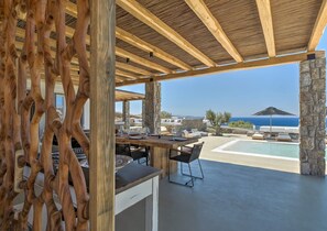 An outdoor dining area with a view of the ocean, stone pillars, and a pool. - Villa With Resort Style Pool (Mykonos)