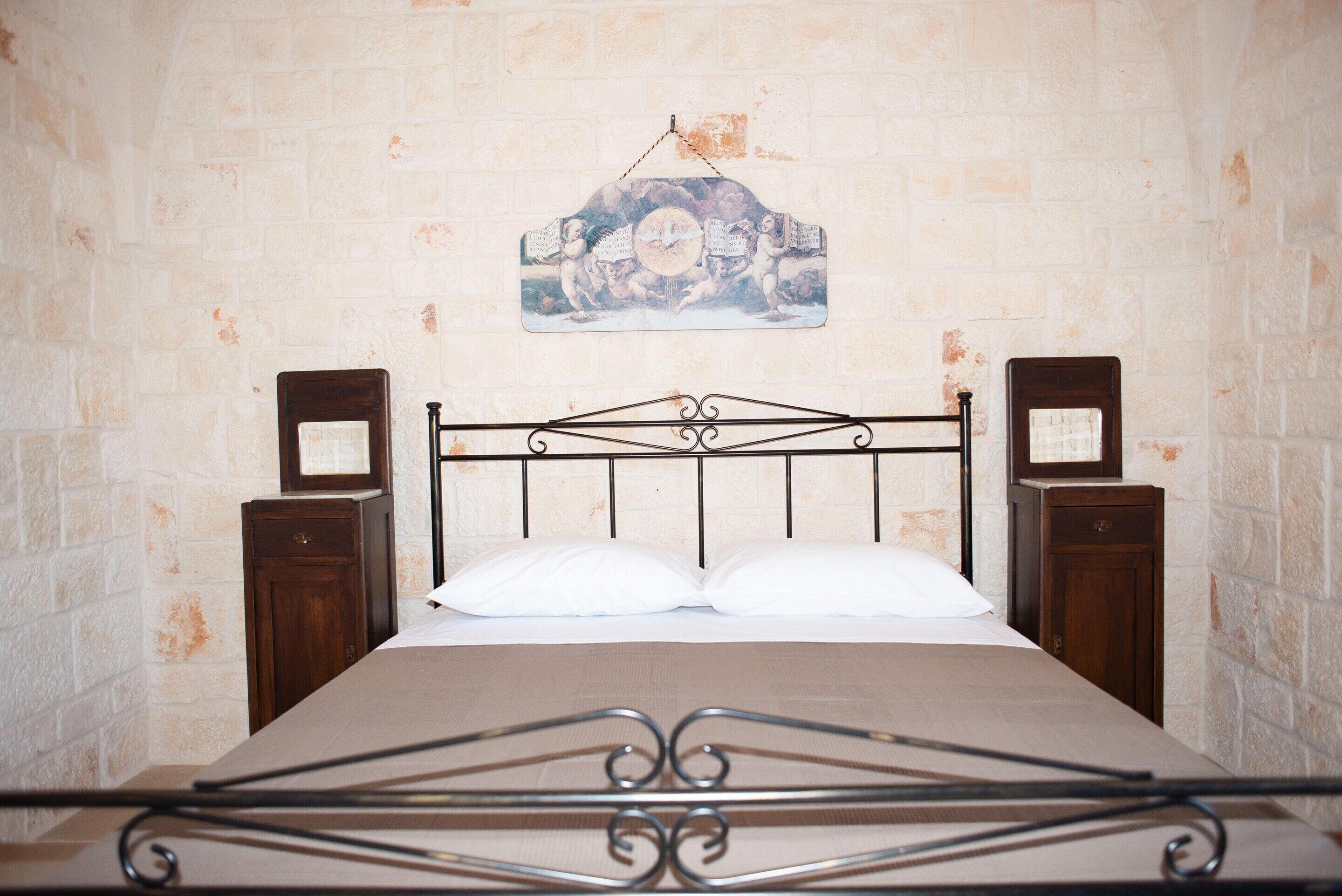 Un lit avec un cadre en métal, des oreillers blancs et une tête de lit en bois. Une œuvre d’art est accrochée au mur au-dessus du lit.