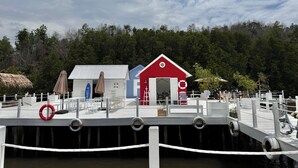 A dock with a red and blue building, a lifebuoy, and a thatched umbrella.