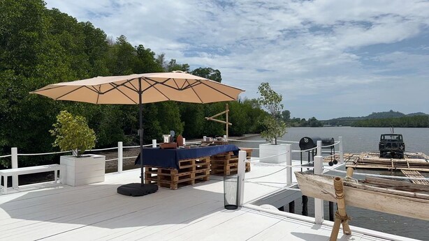 A deck with a table and chairs, a large umbrella, and a boat docked nearby.