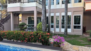 A modern building with a pool, a staircase, and a well-maintained garden with red and pink flowers. - khun mai villa (Pattaya)