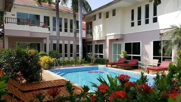 A hotel with a swimming pool surrounded by lounge chairs and tropical plants. - khun mai villa (Pattaya)