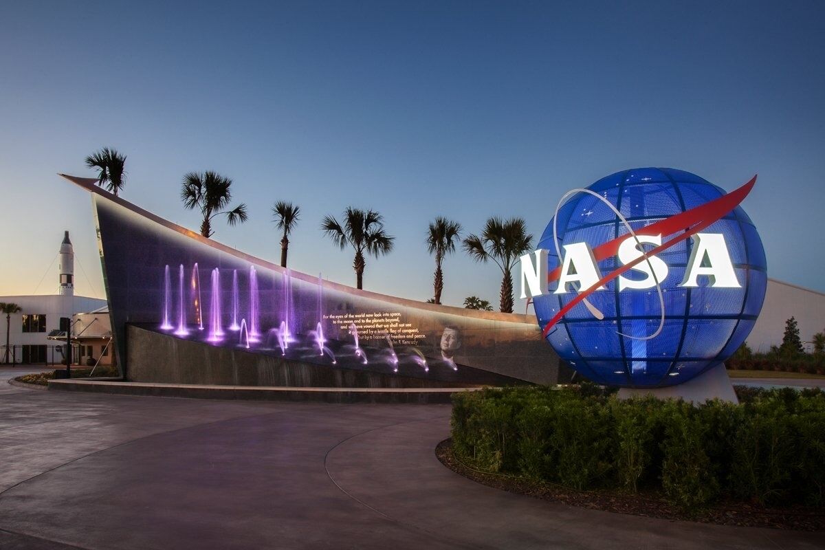 Un bâtiment de la NASA avec une grande sphère bleue et un mur incurvé illuminé de lumières violettes.