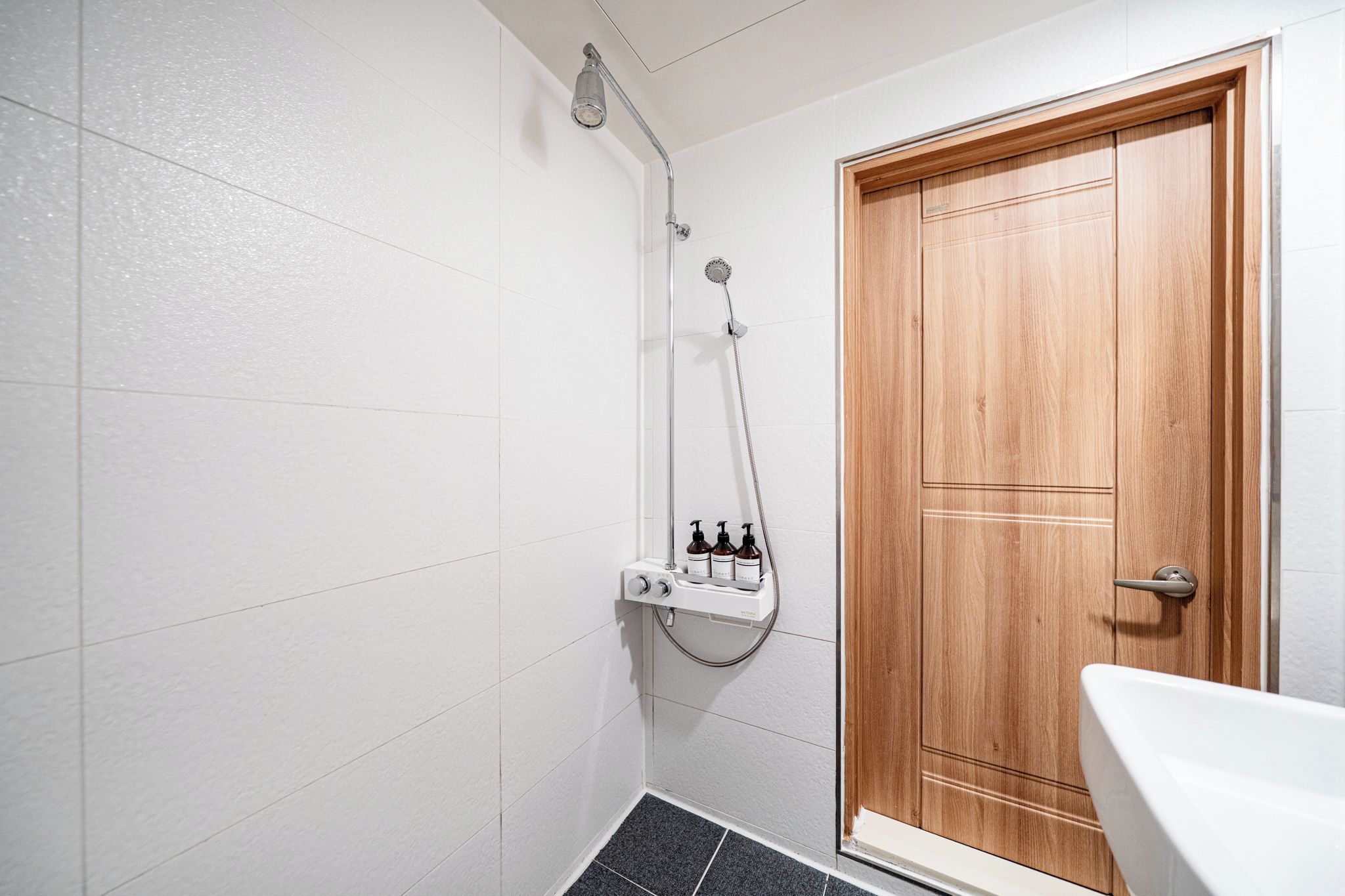 A bathroom with a shower, a wooden door, and a white sink.