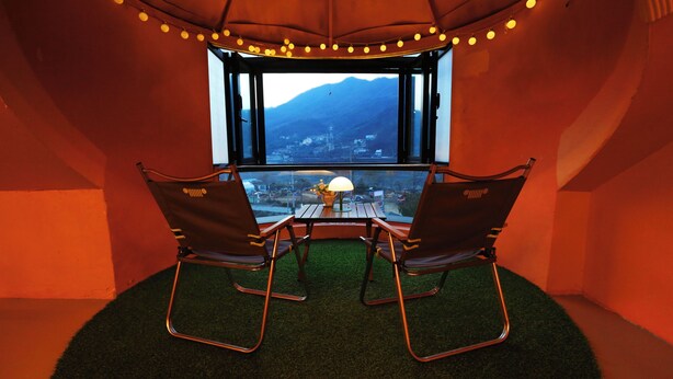 A cozy seating area with two chairs and a table, a lamp, and a view of a cityscape through a window. - Yangpyeong Moonholidarak (Yangpyeong)