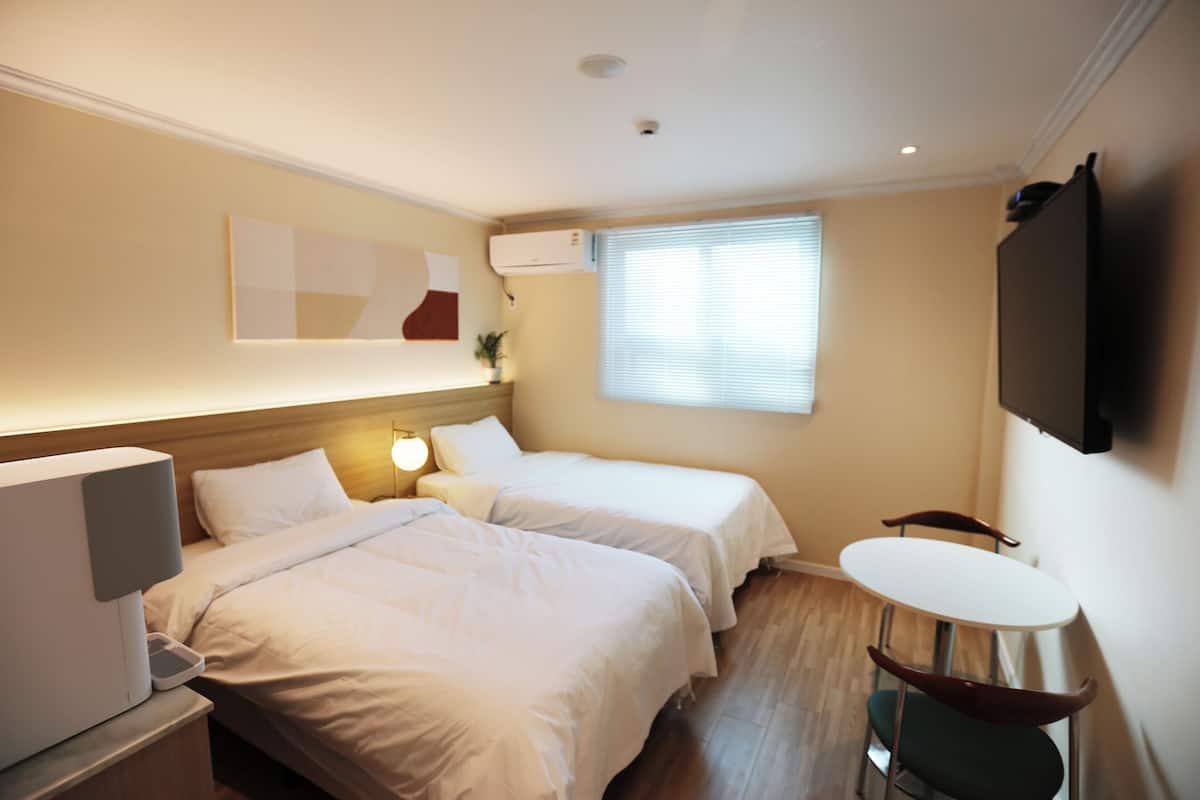 Habitación de hotel con dos camas, un escritorio con ordenador, una mesita pequeña y un televisor montado en la pared.