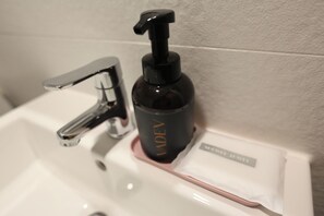 Un lavamanos de baño con un grifo moderno y una botella negra de jabón para manos etiquetada
