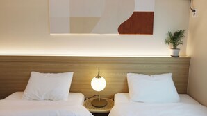 A hotel room with a wooden headboard, two white beds, a round table with a lamp, a wall-mounted air conditioner, and a potted plant. - Yangpyeong Moonholidarak (Yangpyeong)