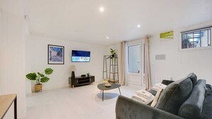 A modern living room with a grey sofa, a small round coffee table, a TV on the wall, and a plant in a basket.