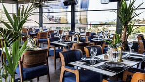 Ravintola, jossa on ruokailuun katetut pöydät, tuolit ja ruukkukasveja.