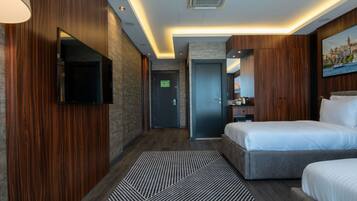 A modern hotel room with a large bed, a flat-screen TV mounted on the wall, a small desk with a lamp, and a painting of a cityscape.