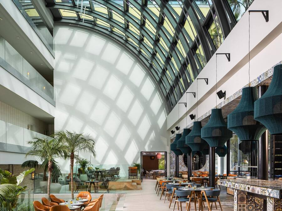 A spacious atrium with a glass ceiling, multiple dining areas, and a central seating area with tables and chairs.