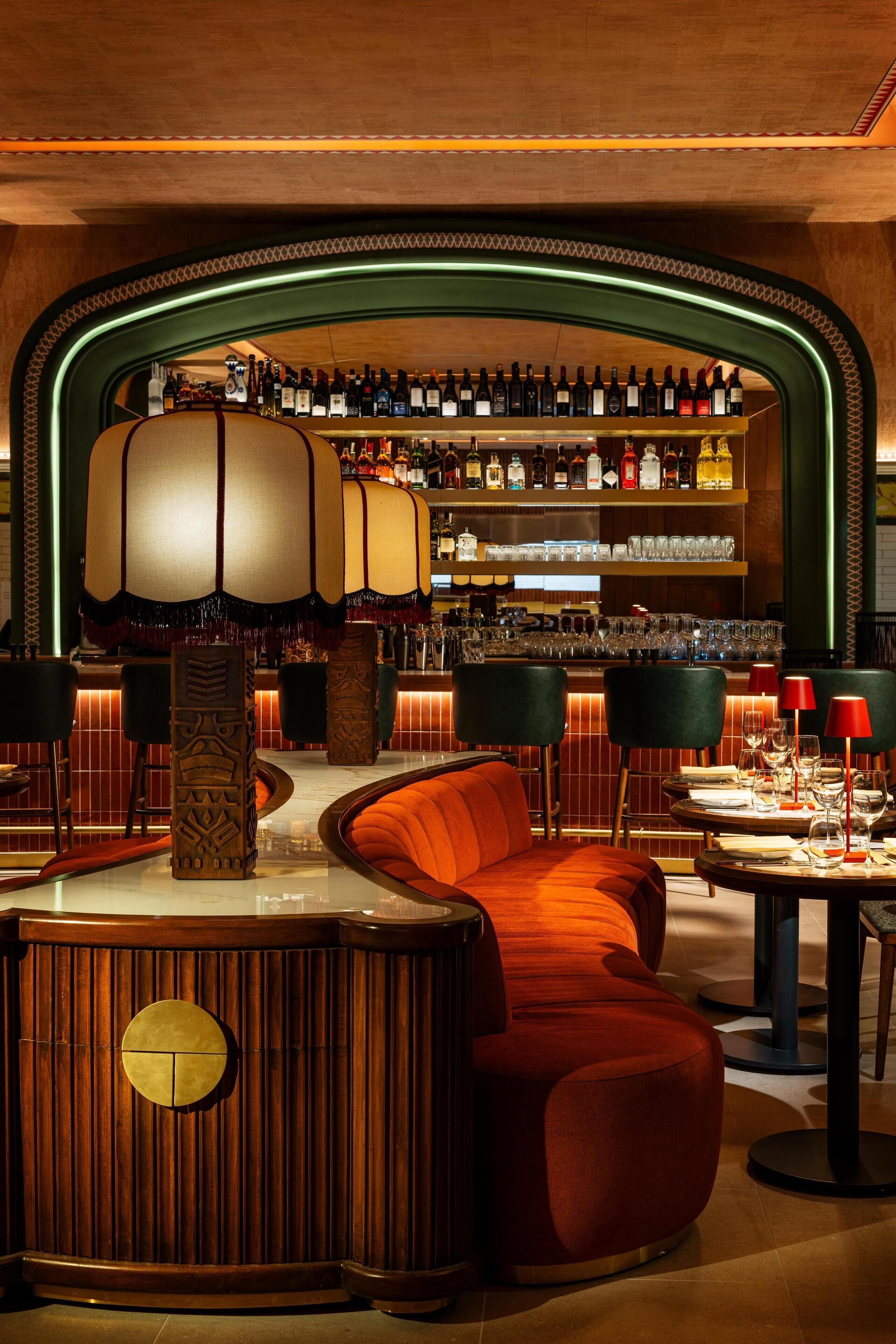 A bar area with a wooden counter, red upholstered seating, and a well-stocked liquor shelf.