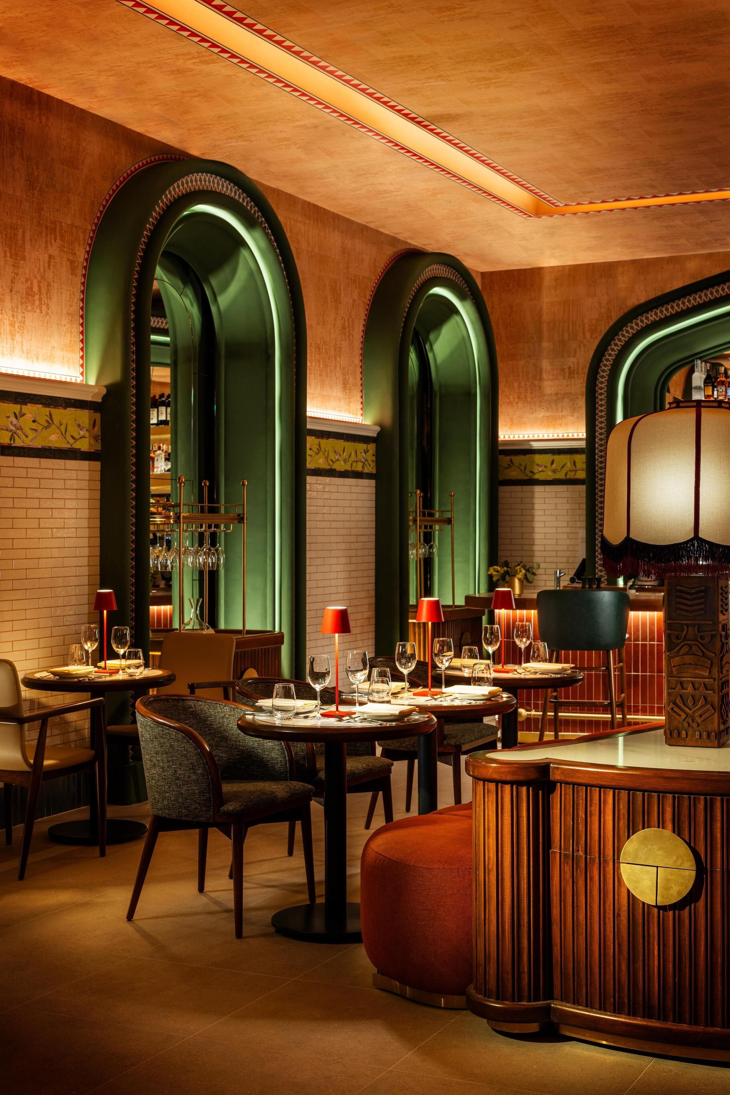 A restaurant with high arched green walls, wooden tables, and red lamps.