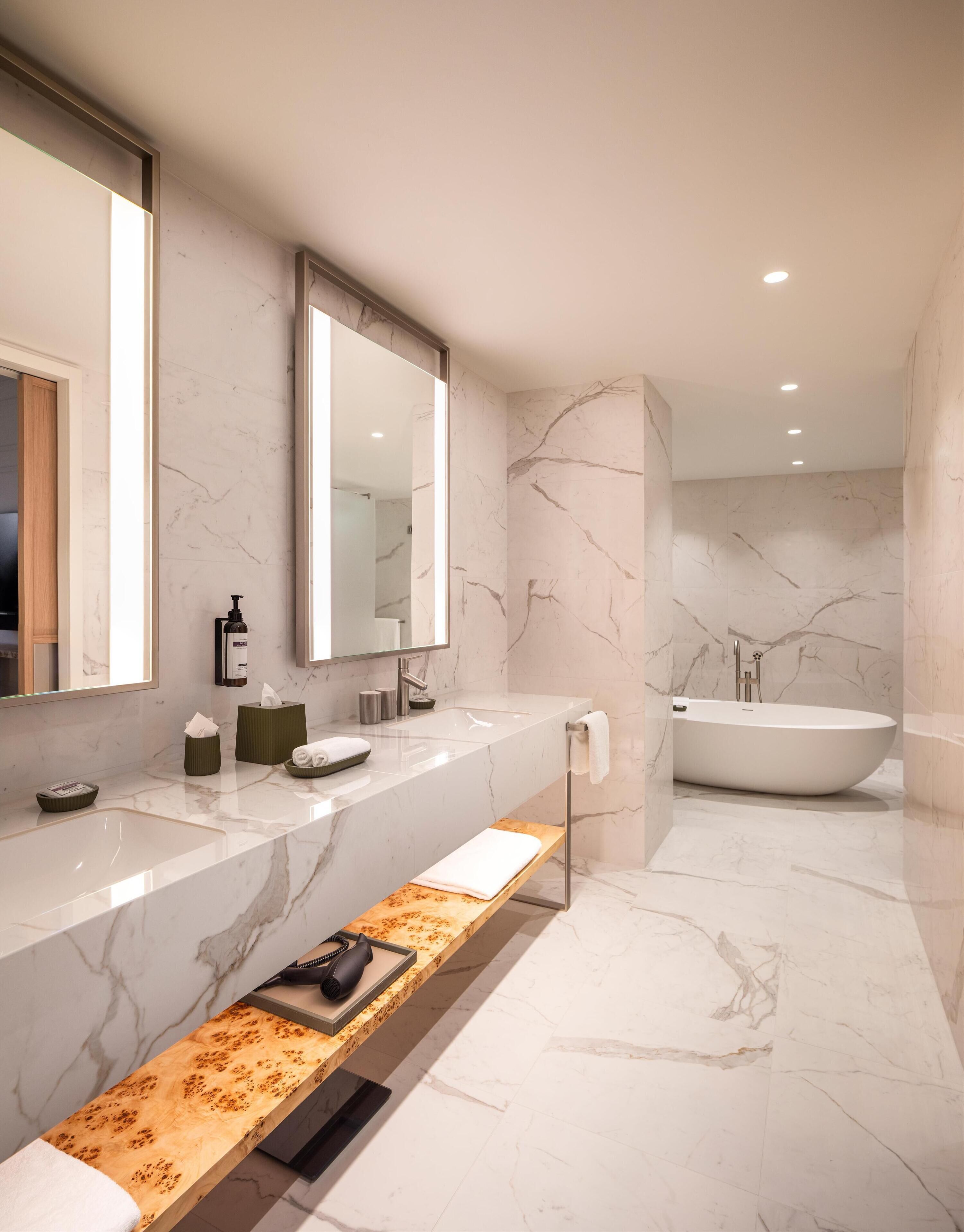 A modern bathroom with a marble vanity, a freestanding bathtub, and a bench.