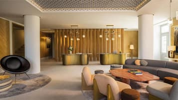 A modern hotel lobby with a central seating area, a reception desk, and a patterned ceiling.
