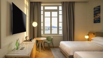 Ett hotellrum med en säng, ett skrivbord med en platt-TV, en stol, ett runt bord och ett fönster med gardiner.