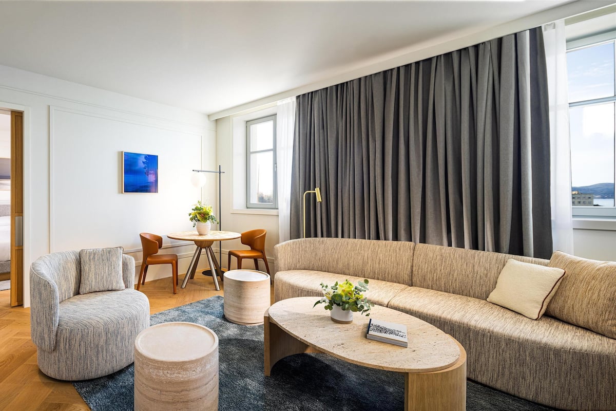 A modern living room with a sofa, armchair, coffee table, and a dining area with a table and chairs.