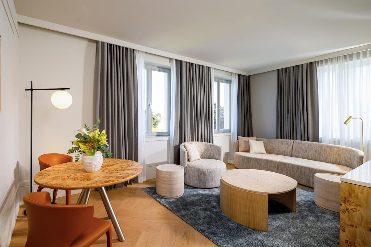 A modern living room with a round wooden table, a sofa, and a chair. There is a vase with flowers on the table.