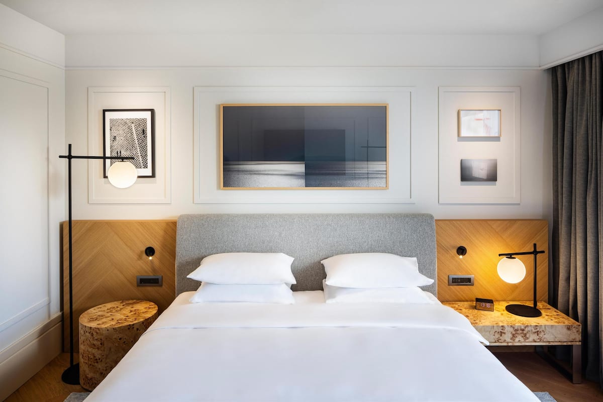A hotel room with a large bed, two bedside tables, a wall-mounted artwork, and a floor lamp.