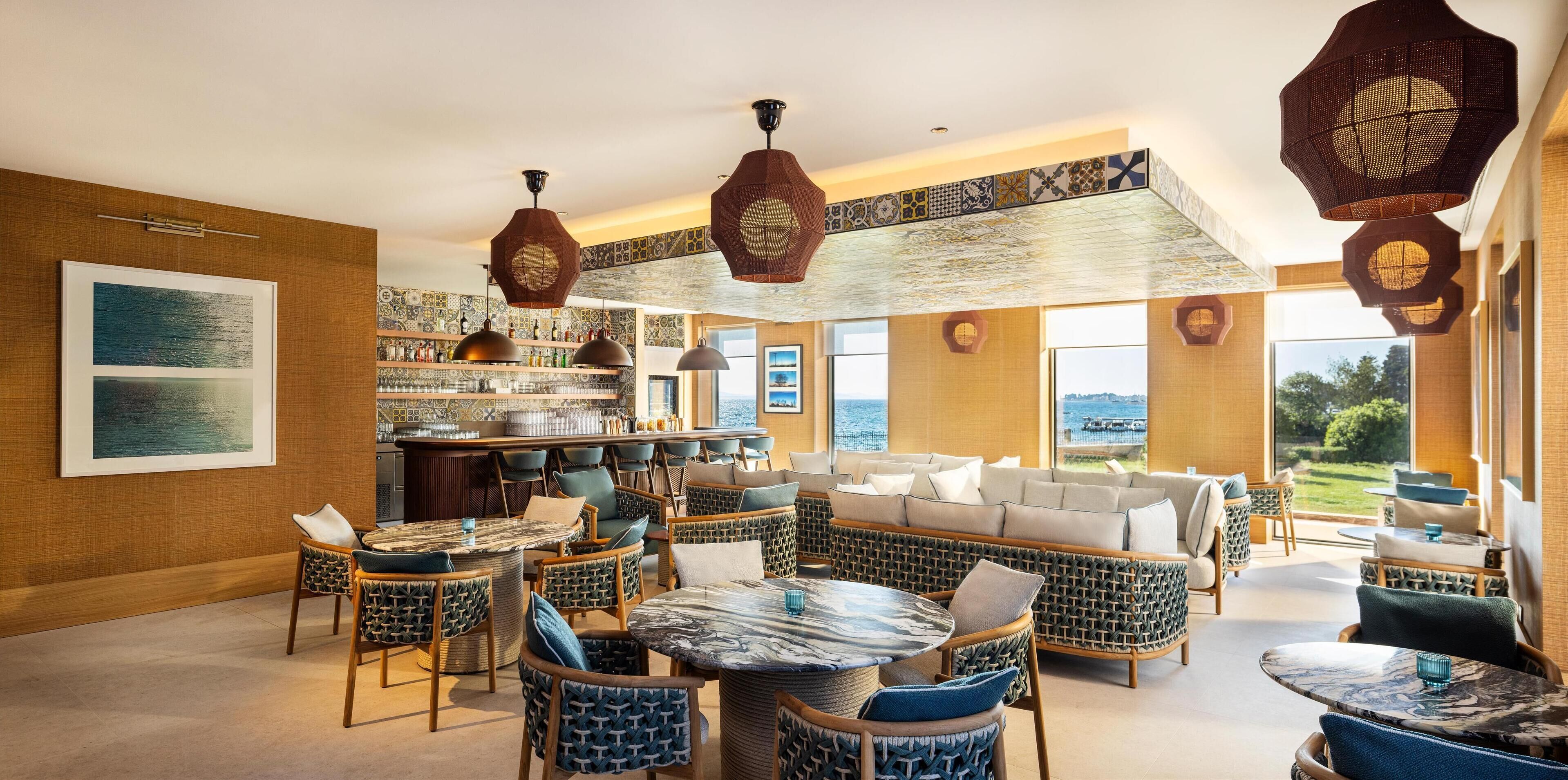A spacious lounge area with wicker furniture, a bar, and large windows offering a view of the outdoors.